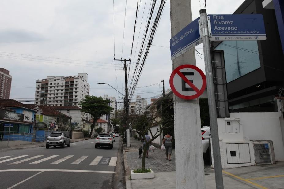 placa de proibido estacionar afixada em poste à direita. Carros passam pela rua. #paratodosverem