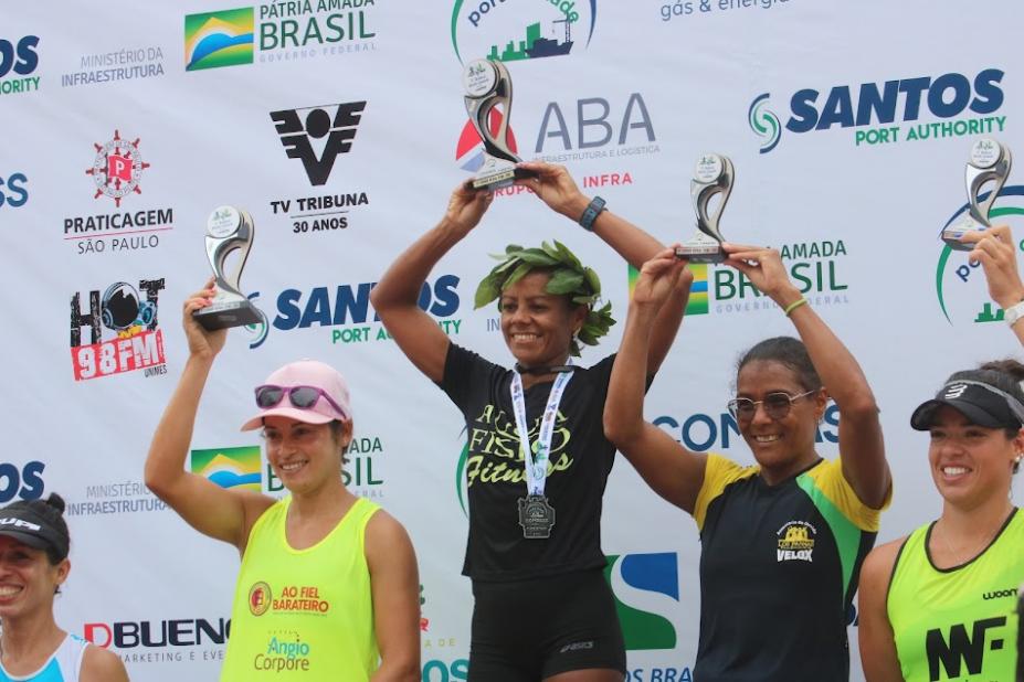 Pódio feminino com Ivanilda Pereira dos Santos ao centro. Elas estão todas com os braços para o alto segurando os troféus. #paratodosverem