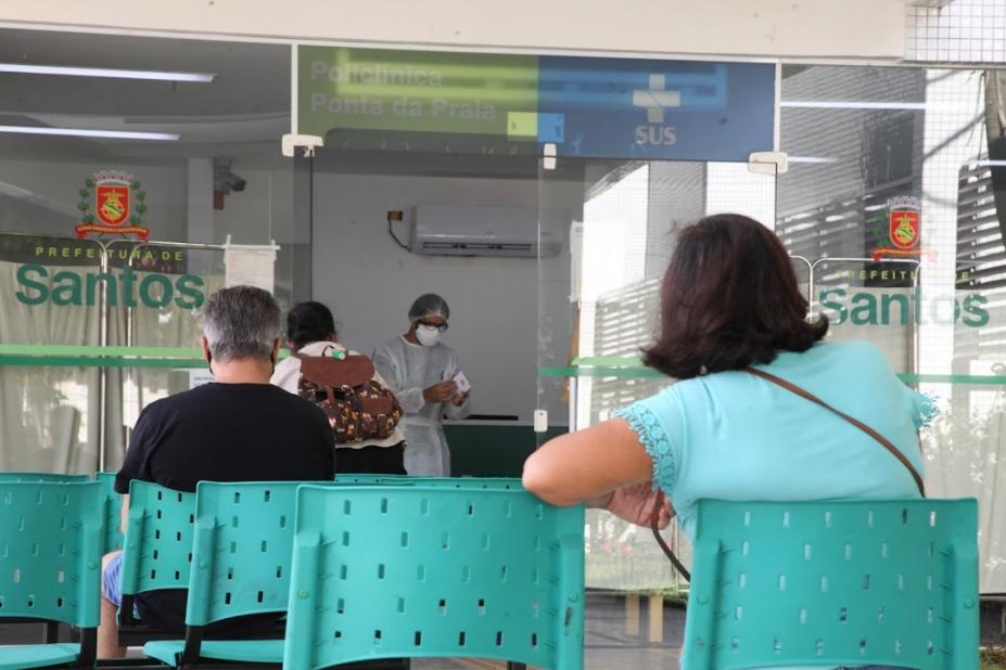 pessoas estão sentadas em cadeiras em policlínica aguardando atendimento. #paratodosverem