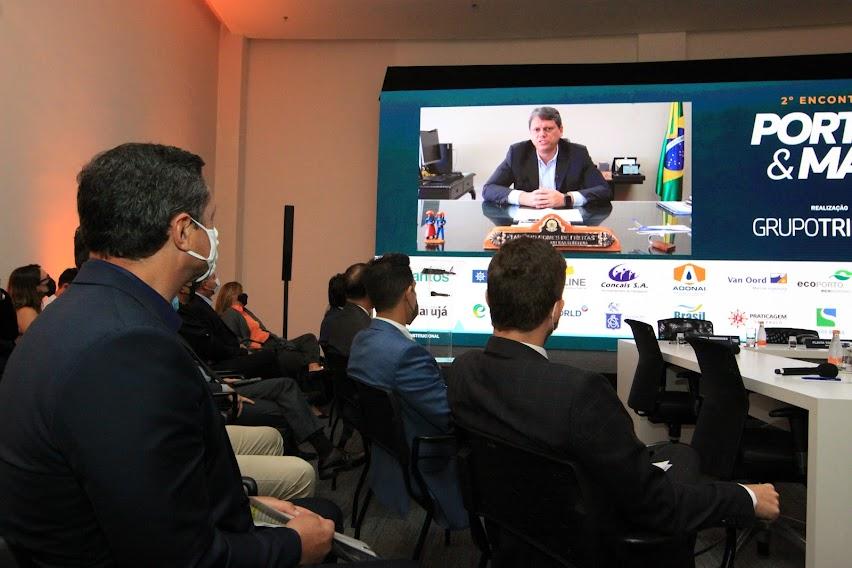 auditório com pessoas sentadas assistindo à apresentação de um ministro no telão. #paratodosverem