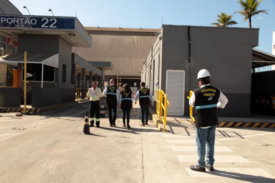 agentes uniformizados e com capacetes estão em frente a um dos portões de entrada de terminal portuário. #paratodosverem
