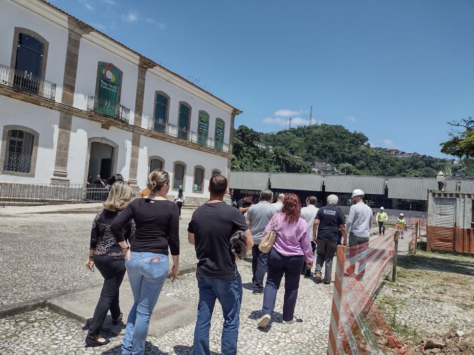 pessoas estão de costas para foto andando em praça e ao lado de obras à direita. #paratodosverem 