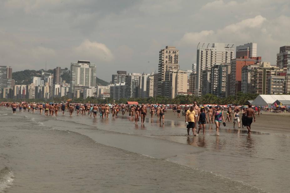 pessoas caminhando na praia à beira d'água. #paratodosverem 