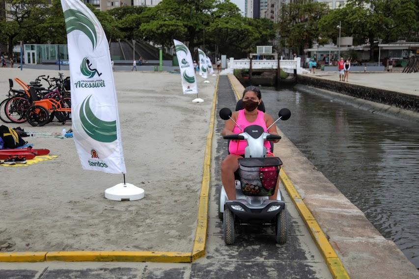 Mulher com veículo adaptado passa pela areia da praia em passarela adaptada #paratodosverem