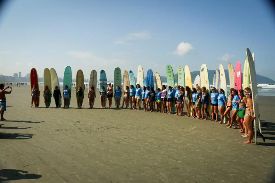 Surfistas estão na areia da praia. Eles posam para foto cada um com sua prancha oca em pé. #Pracegover