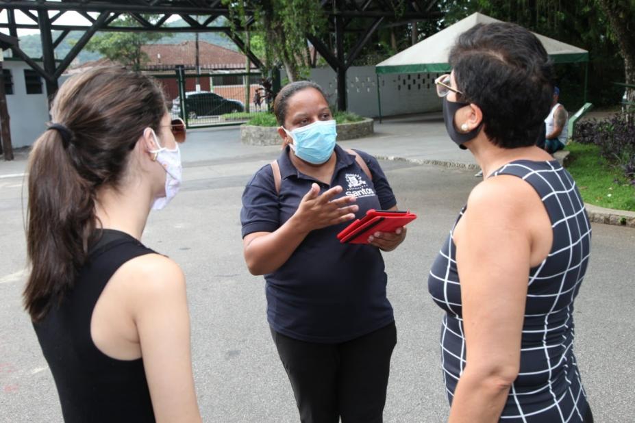 Agente da ouvidoria segura tablet enquanto conversa com duas mulheres em parque. #Paratodosverem