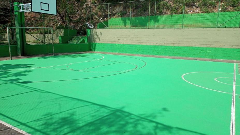 vista geral da quara, com pintura predominante verde, uma quadra de basquete e trave de gol ao fundo. #paratodosverem
