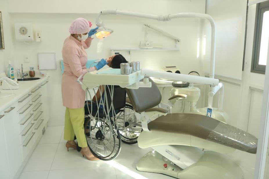 Em um consultório, dentista atende mulher em uma cadeira de rodas. #paratodosverem