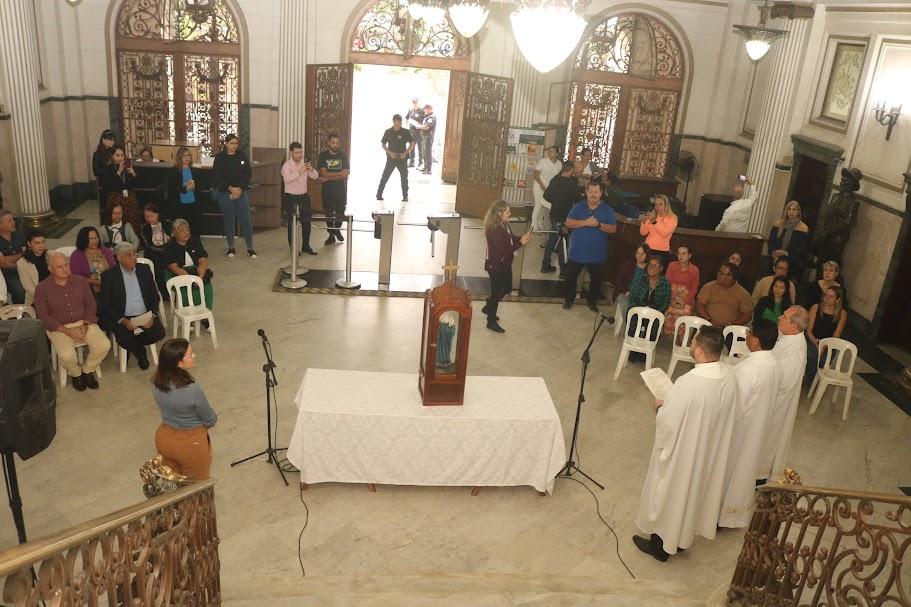 imagem está sobreuma mesa no centro do saguão da prefeitura. Várias pessoas em torno. #paratodosverem 