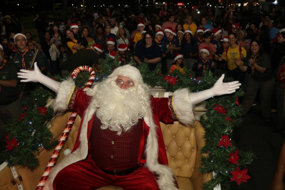 papai noel de braços abertos com grande público ao fundo. #paratodosverem