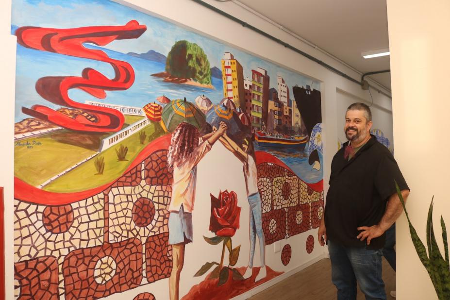 O artista junto com a pintura feita. #Paratodosverem.