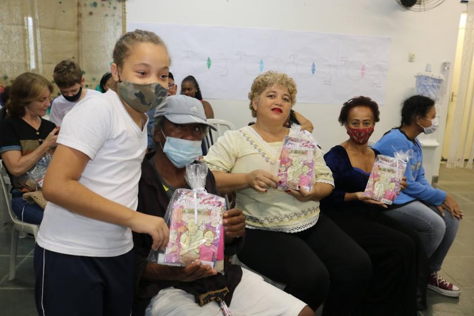 criança ao lado de idosa com presente e mais duas ao lado #paratodosverem