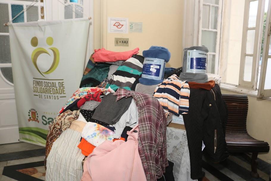 peças de roupas sobre uma mesa ao lado de banner do fundo social de solidariedade. #paratodosverem