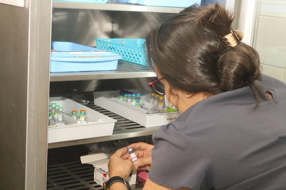 mulher segura frasco de vacina diante de geladeira com porta aberta. #paratodosverem 
