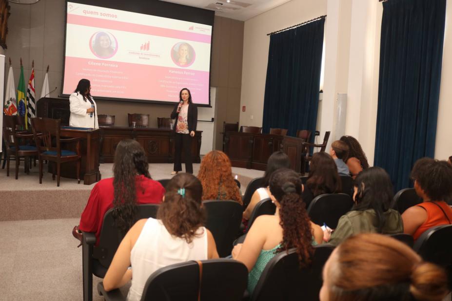 mulheres sentadas em auditório assistem palestra. #paratodosverem 
