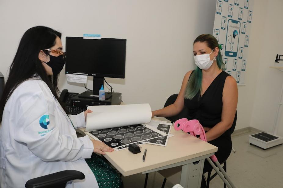 medica está com exame aberto na mesa e atendendo uma mulher. #paratodosverem