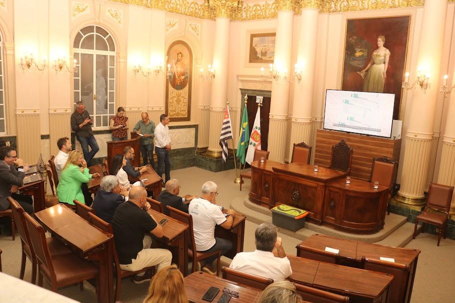 sala princesa isabel com pessoas sentadas assistindo a um vídeo que é reproduzido num telão. #paratodosverem