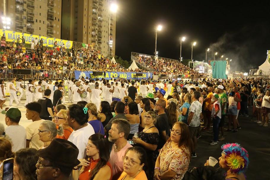 passarela do samba lotada de público com escola passando ao fundo. #paratodosverem 