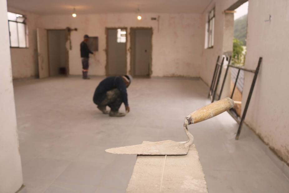 pá de pedreiro em primeiro plano e homens ao fundo. #paratodosverem