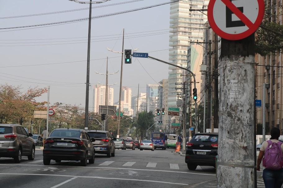 avenida com veículos circulando e semáforos todos em verde, abertos ao fluxo. #paratodosverem 