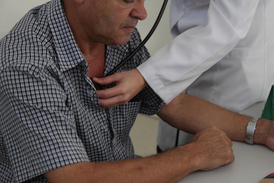 Foto em cluse, com homem sendo auscultado. Mão que segura o 