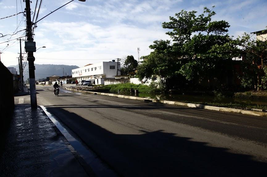 Trecho de avenida asfaltada, com postes do lado esquerdo e calçada com árvores à direita. #Pracegover