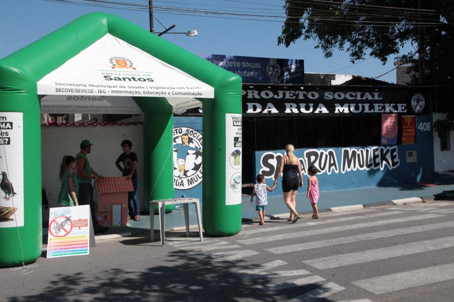 movimento de rua com mãe passeando com dois filhos, à esquerda uma tenda verde e branca