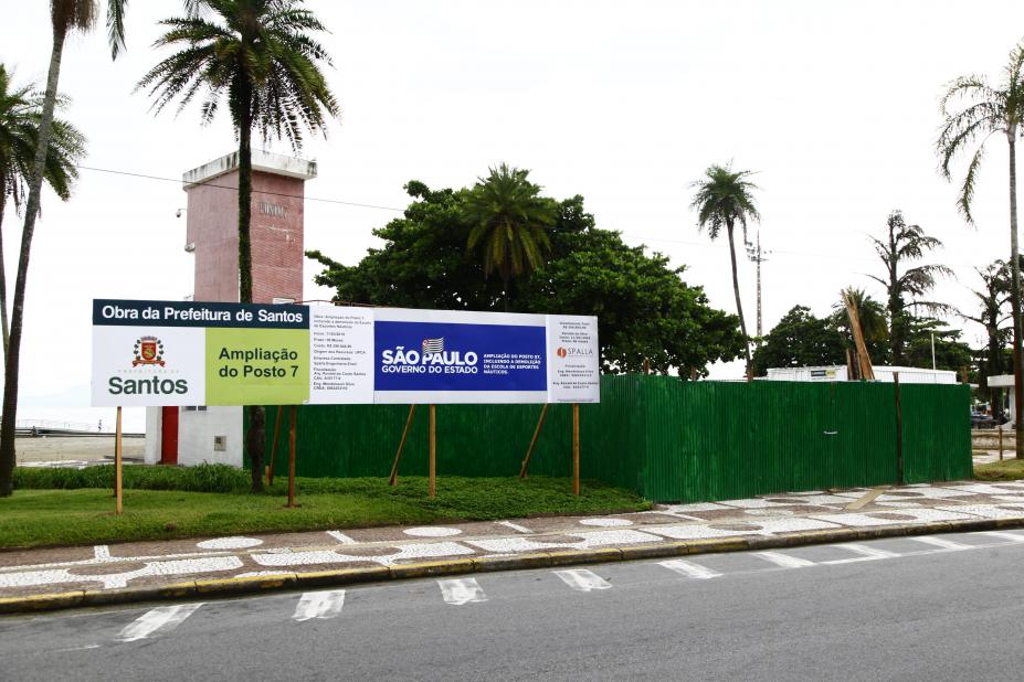 Área do posto de salvamento 7, na orla da praia, com tapume em torno da obra e placa informativa das melhorias. #Pracegover