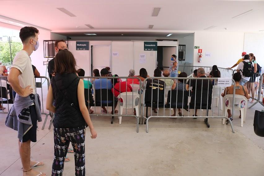 pessoas sentadas em frente a tenda aguardando atendimento cercadas pro gradis #paratodosverem