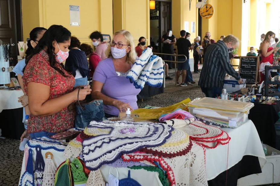 Mulheres olham artesanato em feira #paratodosverem