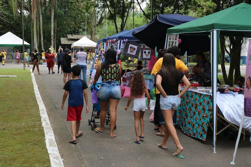 barracas de artesanato em meio a um jardim, com pessoas circulando. #paratodosverem 