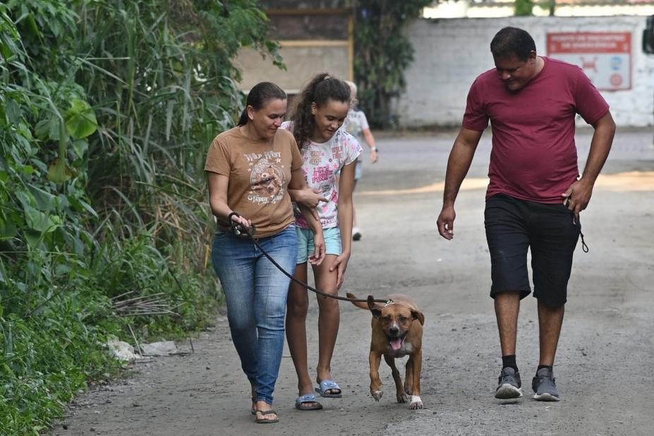 família de três pessoas caminha com cão. #paratodosverem