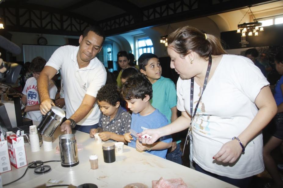 dois monitores ensinam preparação de café e crianças observam #paratodosverem