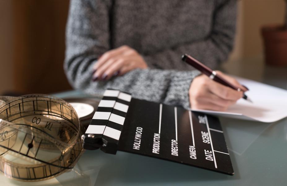 pessoas escreve em mesa com claquete de cinema na mesa #paratodosverem