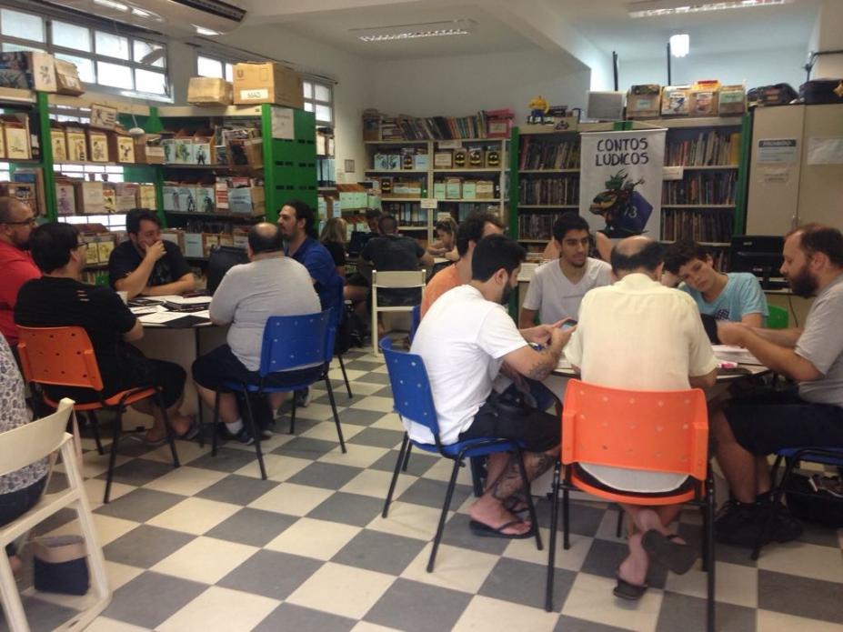 pessoas sentadas em mesas jogam rpg em biblioteca #paratodosverem