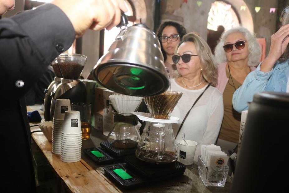 mão seguram bule e servem café para público. #paratodosverem