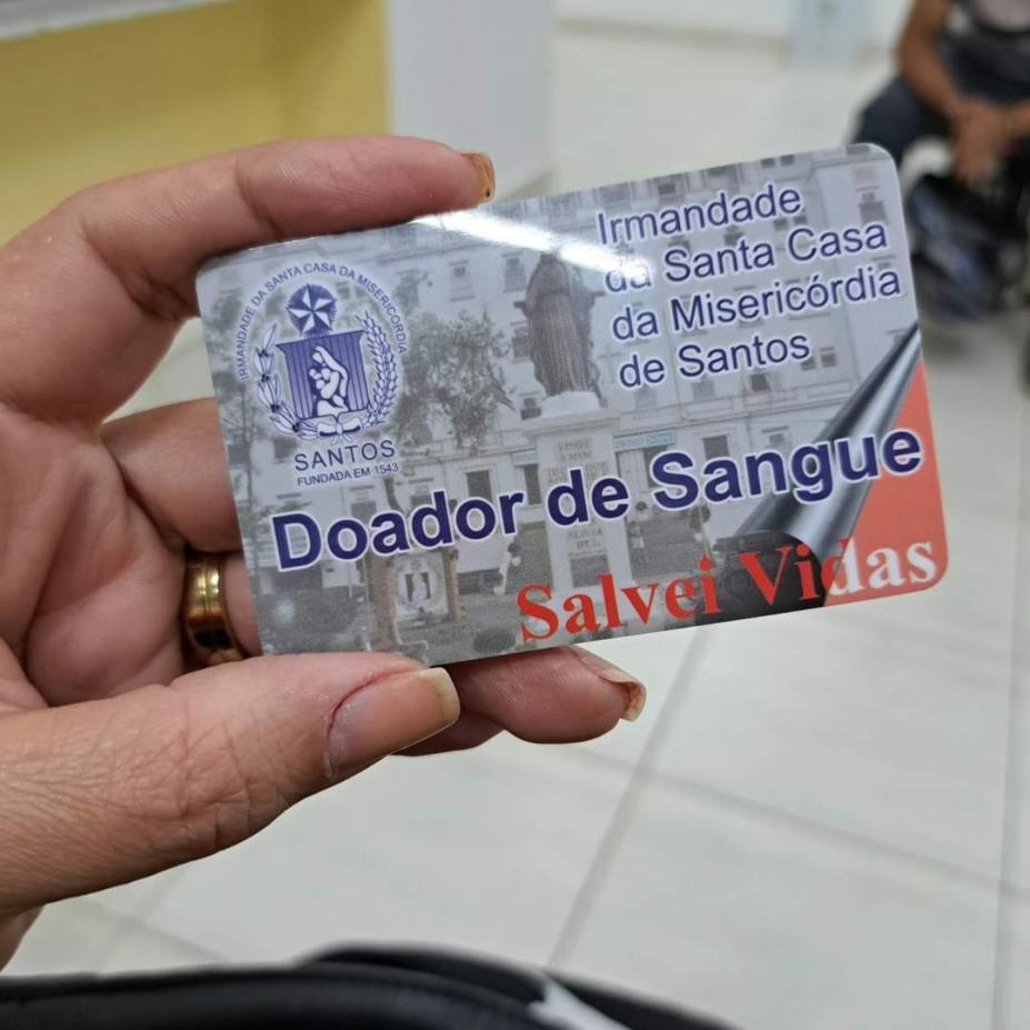 mão segura cartão de doador onde se lê Doador de Sangue. Salve vidas. Há um símbola da Santa de casa de santos no alto. #paratodosverem 