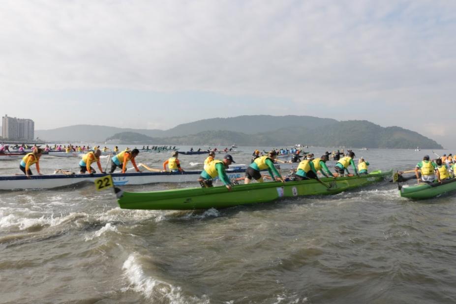 canoas estão entrando no mar com pessoas do lado de fora empurrando-as. São três canoas à vista. #paratodosverem