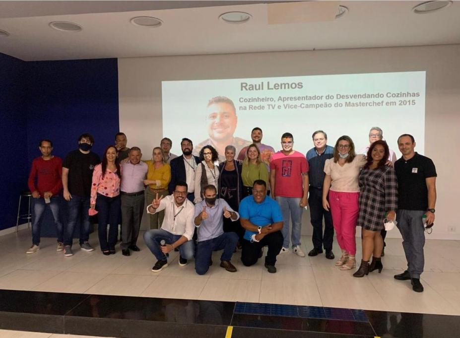 Pessoas posam para foto em cima do palco com telão ao fundo #paratodosverem