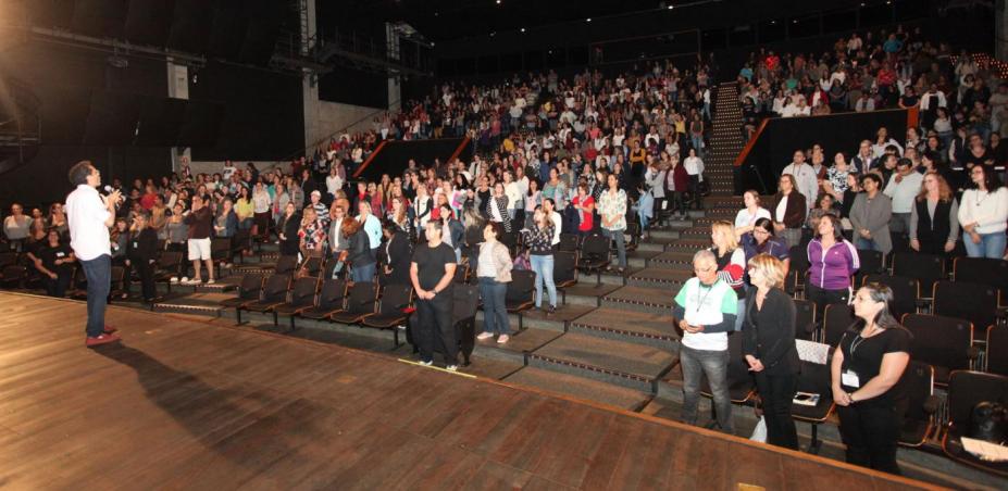 Palestrante no palco do Teatro do Sesc com plateia repleta de educadores. #paratodosverem