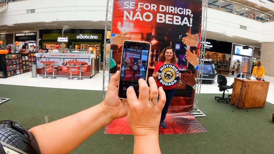 Mulher segura placa com a inscrição Motorista da Roda, embaixo de grande letreiro. #paratodosverem