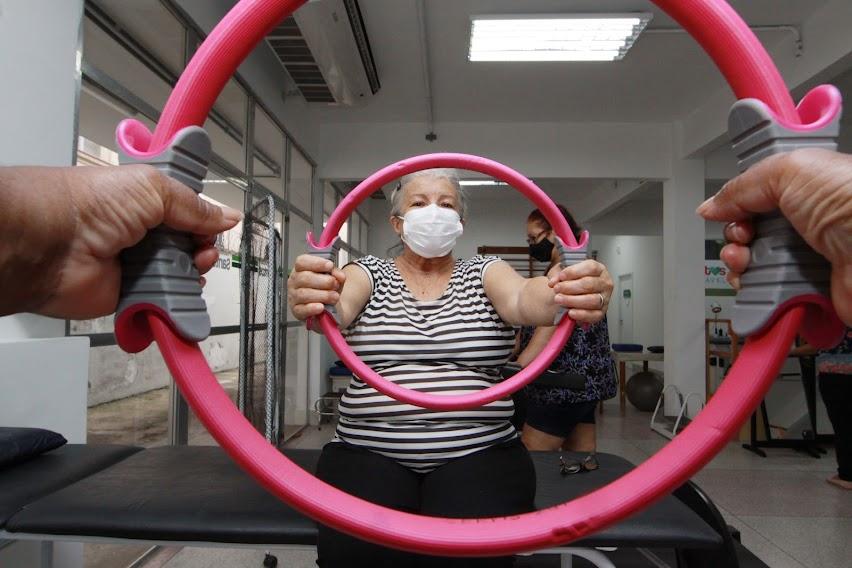 mãos seguram arcos flexíveis em primeiro plano. Ao fundo, uma mulher também segura um arco. A foto faz um efeito de dois círculos distantes, mas parecendo um menor que o outro. #paratodoverem