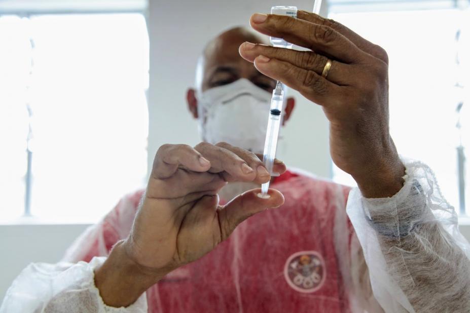 homem insere conteúdo de frasco de vacina em seringa. Ele usa máscara e avental