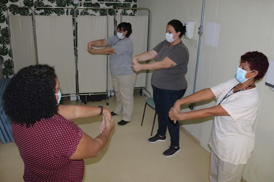 mulheres estão fazendo exercícios de alongamento com os braços em sala. #paratodosverem
