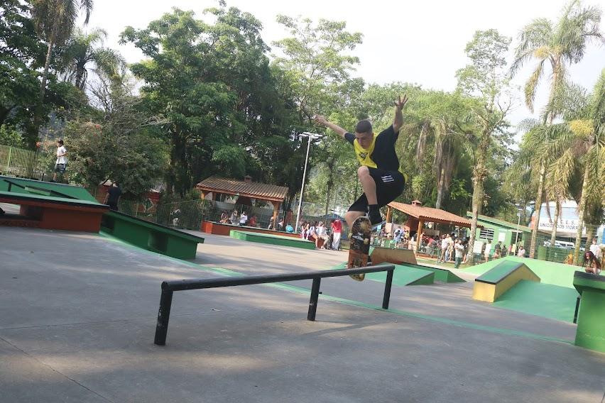 jovem faz manobra em uma espécie de corrimão próprio para skate. ele esta no ar, com os braços para cima. #paratodosverem