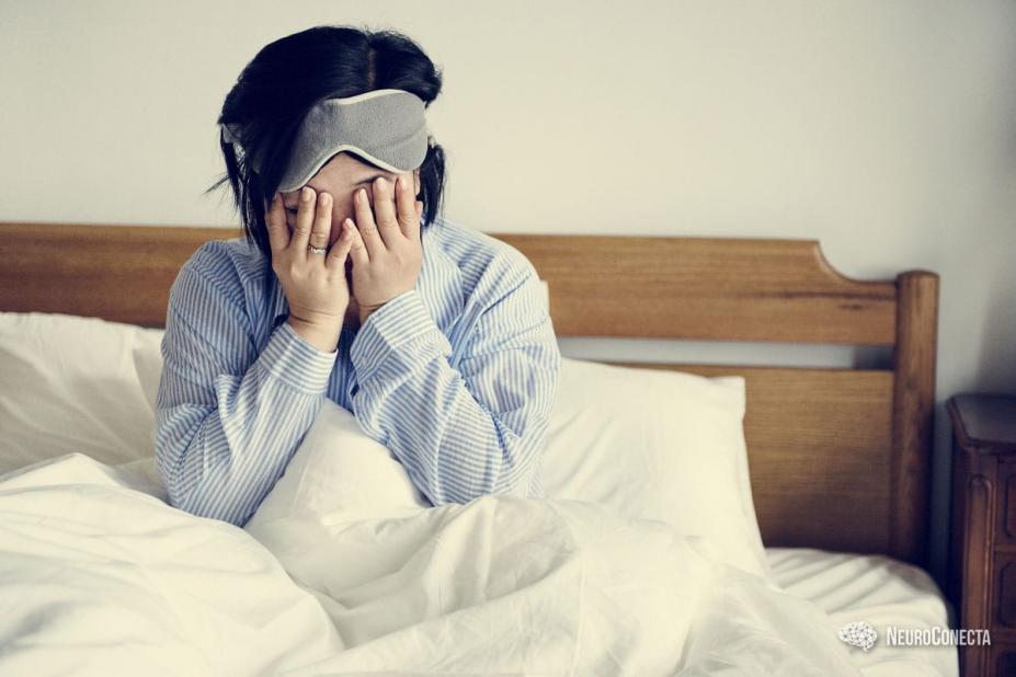 mulher está sentada na cama com as mãos cobrindo o rosto. O tapa olho está na testa. #paratodosverem