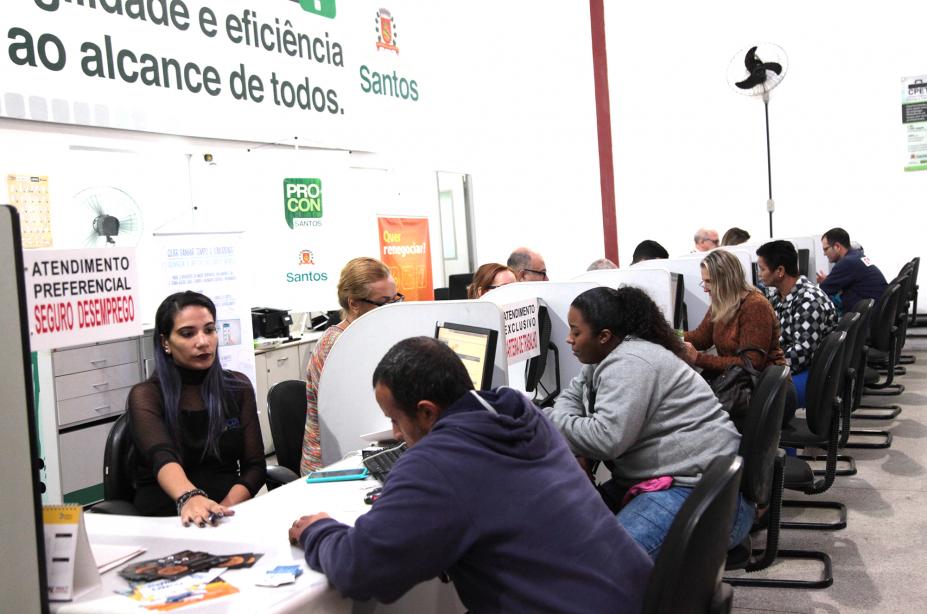 Balcão de atendimento durante mutirão. Várias pessoas estão sentadas diante de recepcionistas. #Pracegover