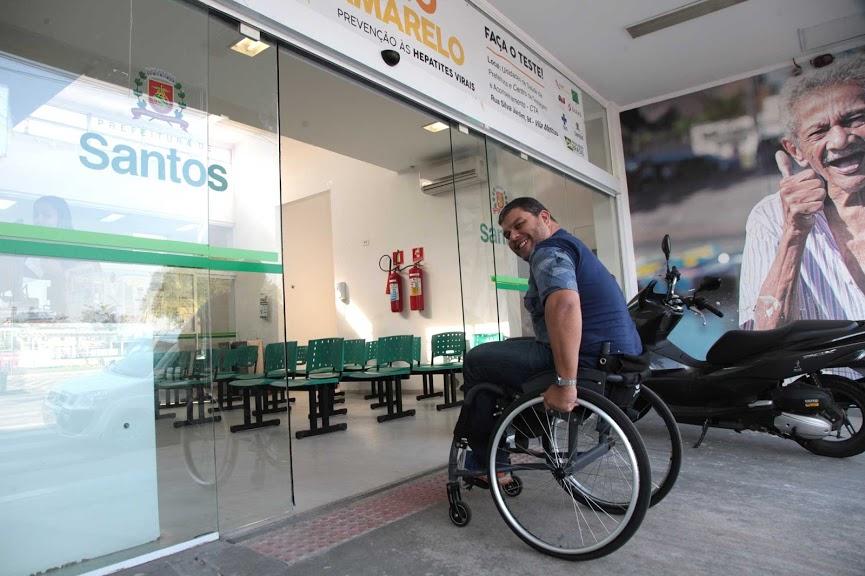 Cadeirante ingressa em policlínica com facilidade, por meio de rampa acessível e porta larga. No solo também há piso tátil. #Pracegover