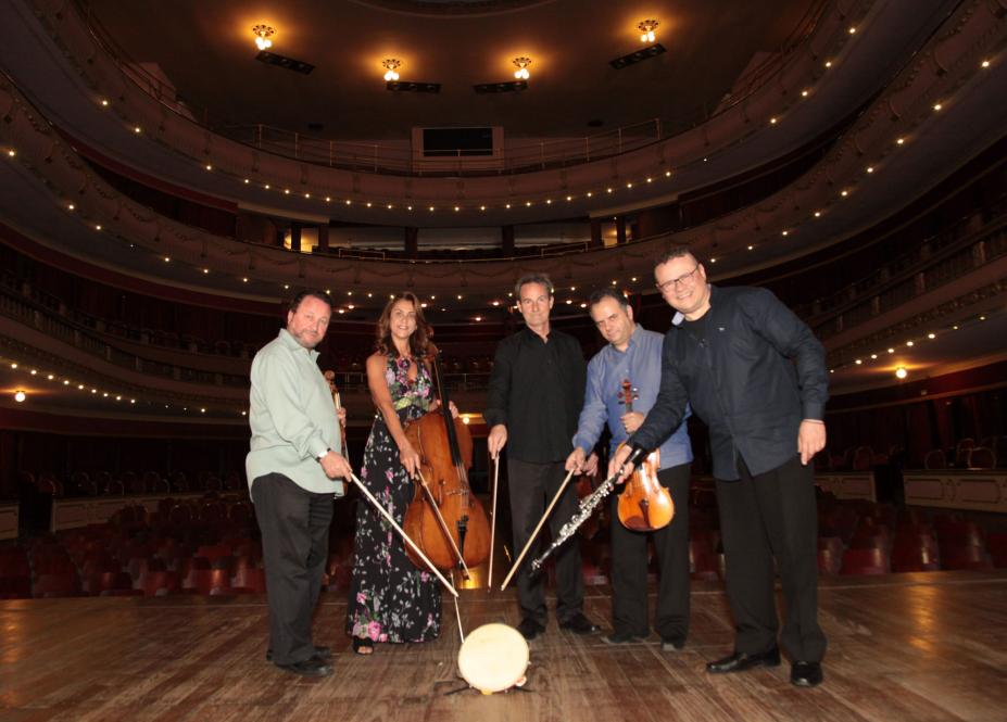 O quarteto e mais um acompanhante. Eles estão em um palco. Todos seguram os arcos de seus instrumentos. #Pracegover