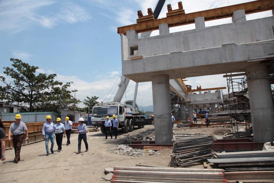 Várias pessoas estão caminhando e observando estrutura de concreto de futura ponte. #Pracegover